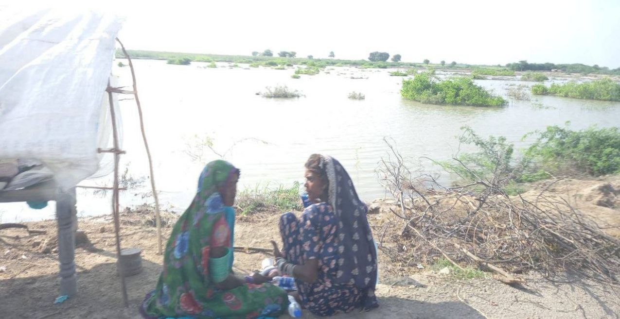 Two women sitting by a bed which has been overturned to create a temporary shelter after their homes were flooded in. (Credit: AFWA Pakistan)
